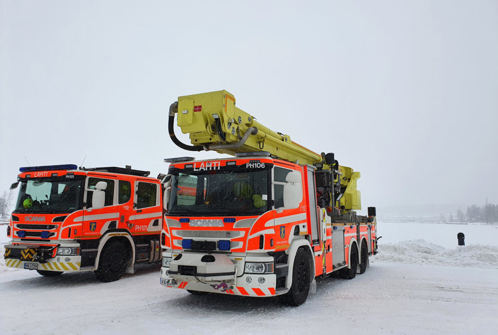 Kaksi punaista paloautoa lumisessa maisemassa. Toisella autoista nosturi katolla. Keulassa teksti Lahti.