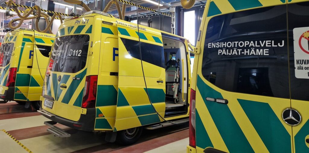 Keltavihreitä ambulansseja tallissa. Takaikkunassa teksti ensihoitopalvelu, Päijät-Häme.